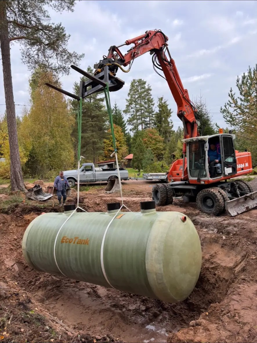 Hjulgrävmaskin sänker ner en ny tank i en grävd grop vid installation i Olsnäs Fäbod